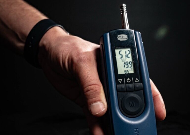 Eine Hand hält ein blaues digitales Atemalkoholmessgerät mit einem Bildschirm, auf dem die Messwerte, einschließlich der Zahl 5,12, vor einem dunklen Hintergrund angezeigt werden - ideal für Aufgaben wie die Wasserschadenortung, bei denen präzise Messungen entscheidend sind.