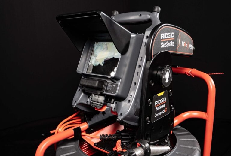 Eine Nahaufnahme eines RIDGID SeeSnake Compact2 Inspektionskamerasystems, ideal für die Wasserschadenortung, mit einem Monitor, der ein Bild anzeigt, aufgerollten orangen Kabeln und einem dunklen Hintergrund.