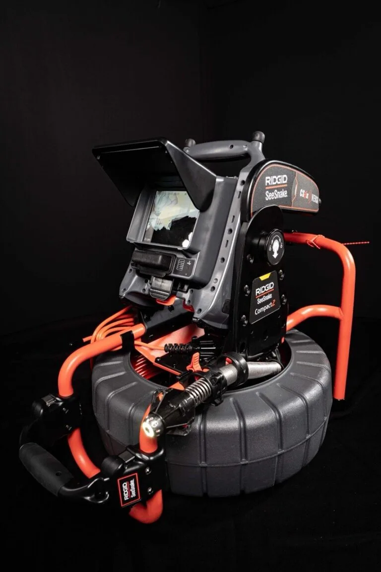 Ein RIDGID SeeSnake Compact2-Rohrinspektionskamerasystem auf dunklem Hintergrund, das den Monitor, das Spiralkabel, die Steuereinheit und den stabilen Rahmen mit orangefarbenen Griffen zeigt - ideal für die präzise Wasserschadenortung bei Inspektionen von Rohrleitungen.