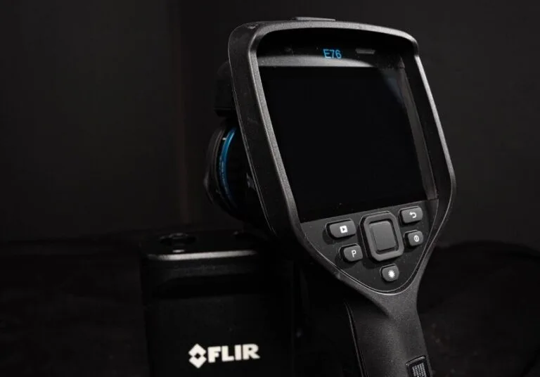 Eine Nahaufnahme einer FLIR E76-Wärmebildkamera mit schwarzem Gehäuse, das angewinkelt ist, um den Bildschirm und die Bedientasten vor einem dunklen Hintergrund zu zeigen - ideal für präzise Wasserschadenortungsanwendungen.