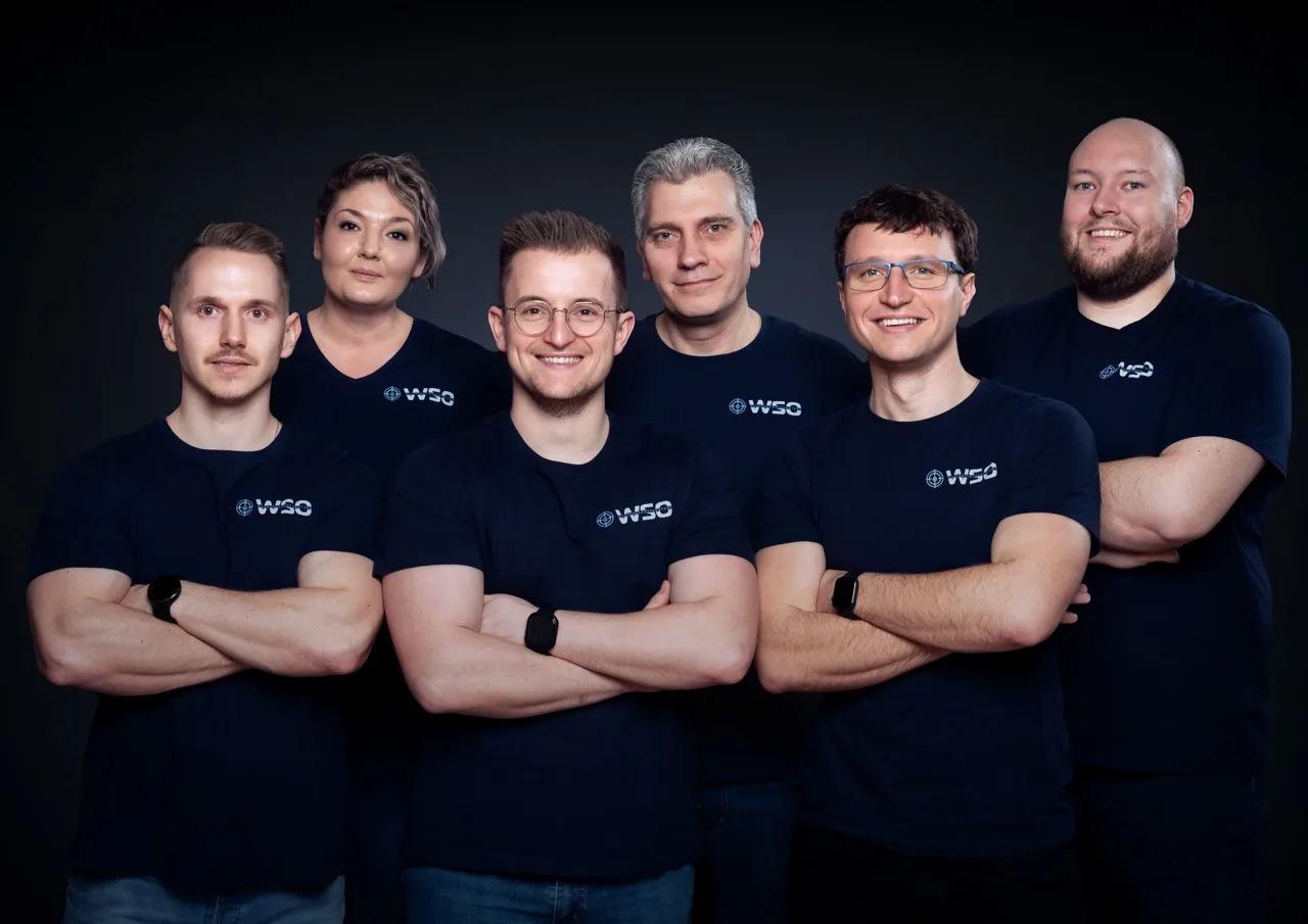 Sechs Personen stehen in zwei Reihen zusammen, alle tragen marineblaue Hemden mit dem WSO-Logo und lächeln selbstbewusst mit verschränkten Armen. Als erfahrenes Team der Wasserschadenortung posieren sie vor einem dunklen Hintergrund, bereit, sich jeder Herausforderung eines Wasserschadens zu stellen.